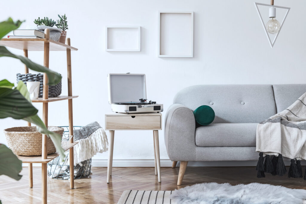 Step 2 Buena Vista Home Valuation: Stylish and cozy scandinavian white interior with design sofa, bookstand with accessories, pillows, blanket, gramophone and mock up photo frames. White background walls and modern triangle lamp.